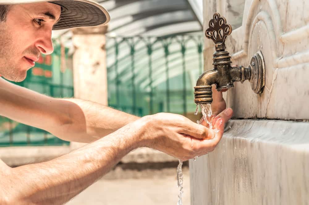 Man drinking roadside tap water with his hand
